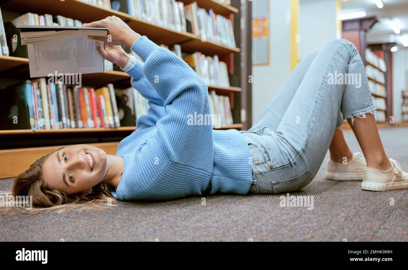 Ritratto, donna sul pavimento e la lettura in biblioteca, rilassarsi e imparare con il sorriso, hobby o l'istruzione superiore. Ragazza studentesca o signora con libro Foto Stock