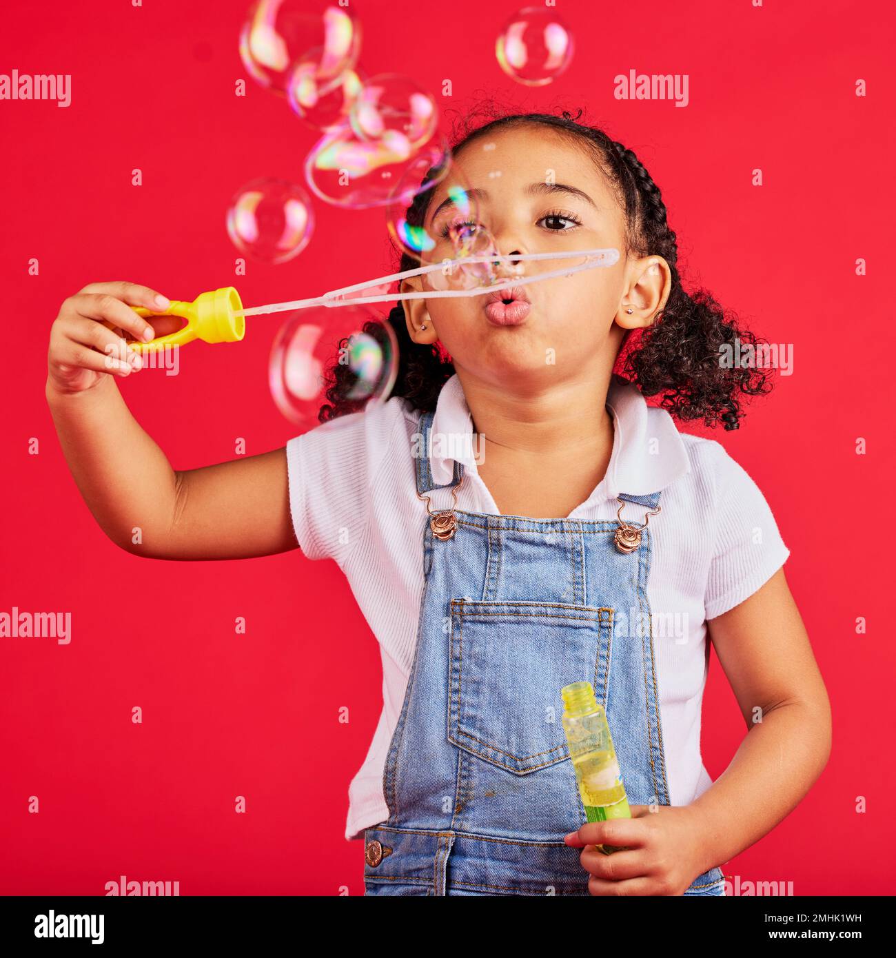 Bambina, giocando o soffiando bolle su sfondo rosso isolato in coordinazione occhio mano, attività o gioco divertente. Bambino, bambino o giovane con sapone, bacchetta Foto Stock