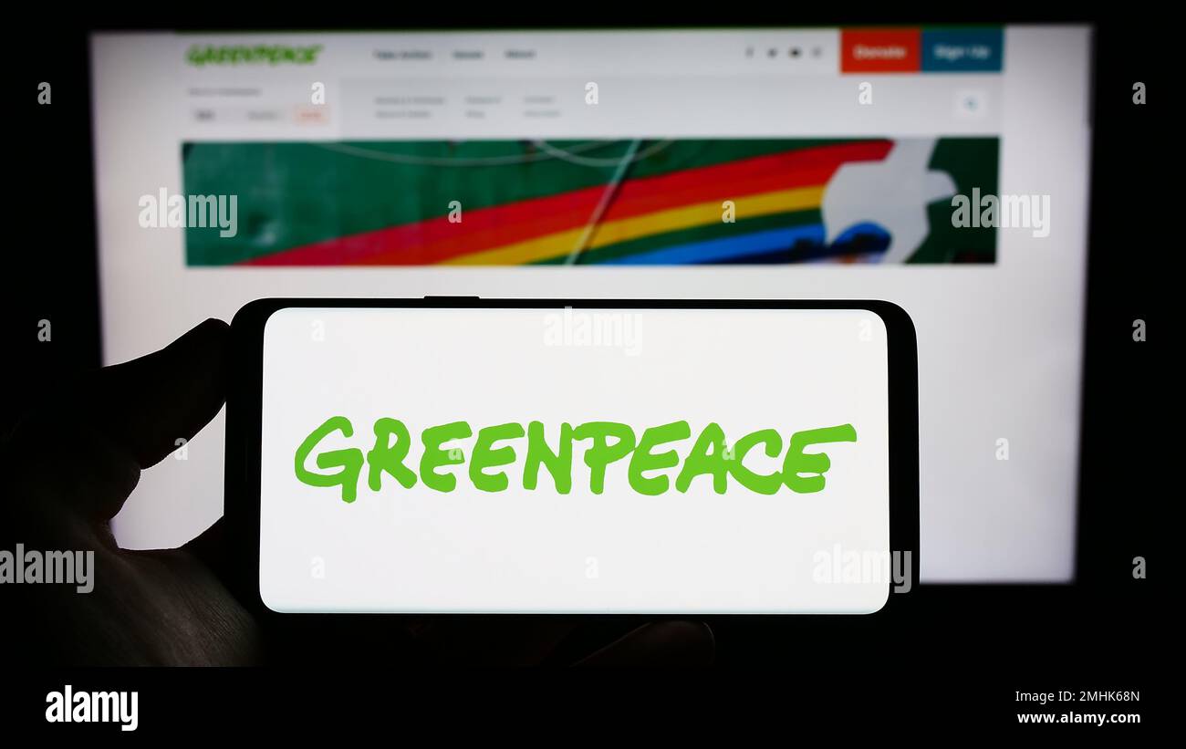 Persona che tiene il telefono cellulare con il logo della campagna ambientale rete Greenpeace sullo schermo di fronte al sito web. Messa a fuoco sul display del telefono. Foto Stock