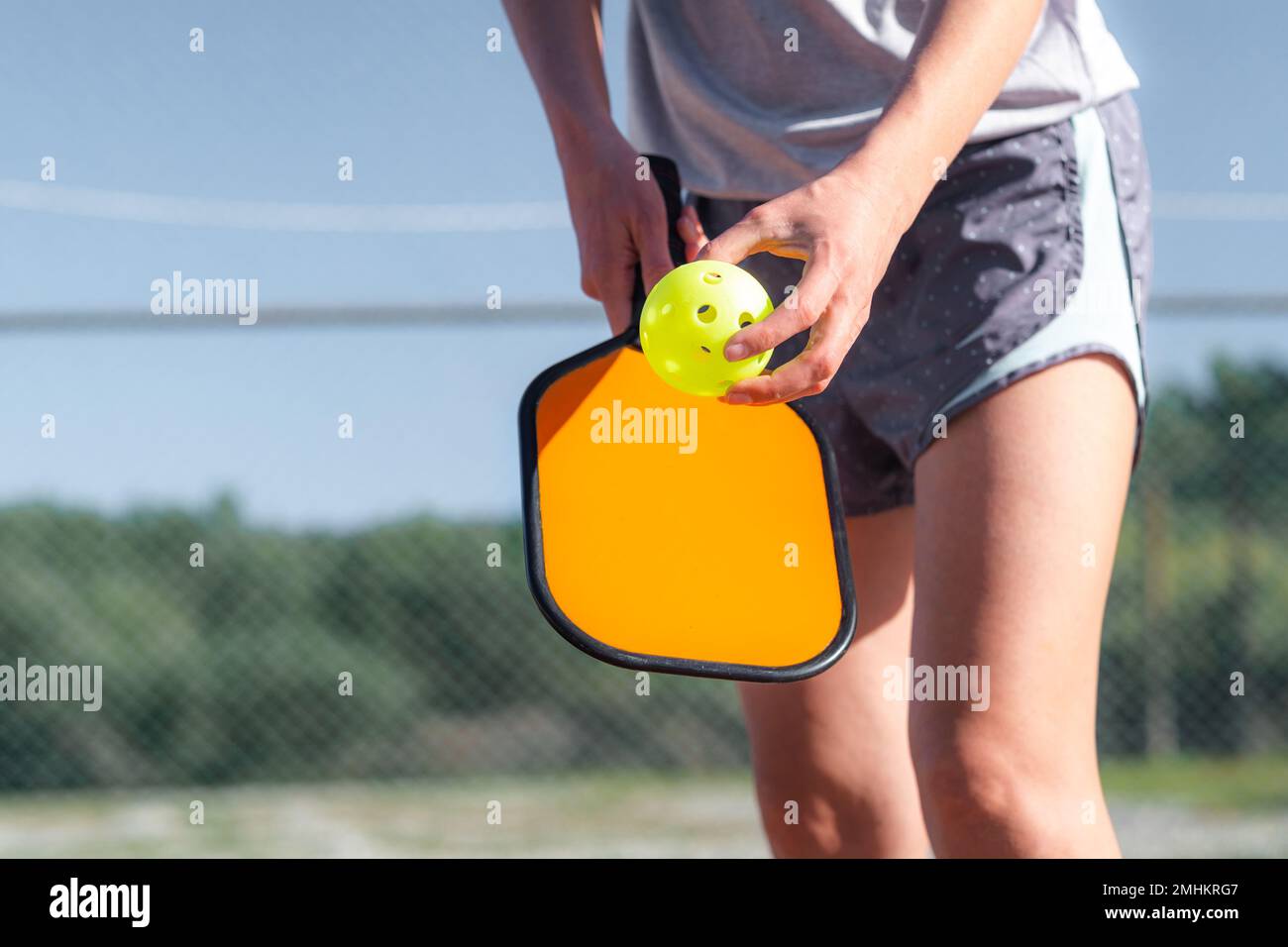 Pickleball paddle e palla gialla primo piano, donna che gioca a pickleball, colpire palla gialla con paddle, attività sportive all'aperto. Foto Stock
