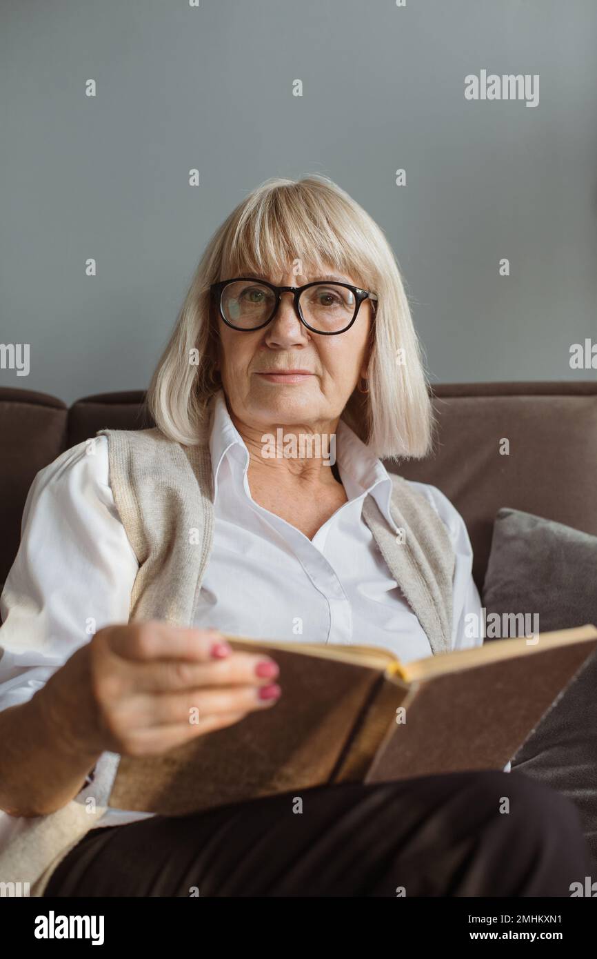 Ritratto di donna anziana rilassata seduta sul divano con libro Foto Stock
