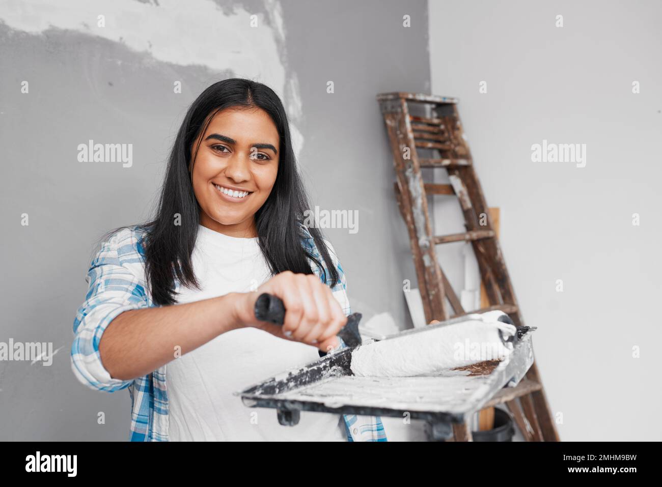 Una donna indiana attraente sorride mentre circa per verniciare la parete con il pennello ed il vassoio Foto Stock