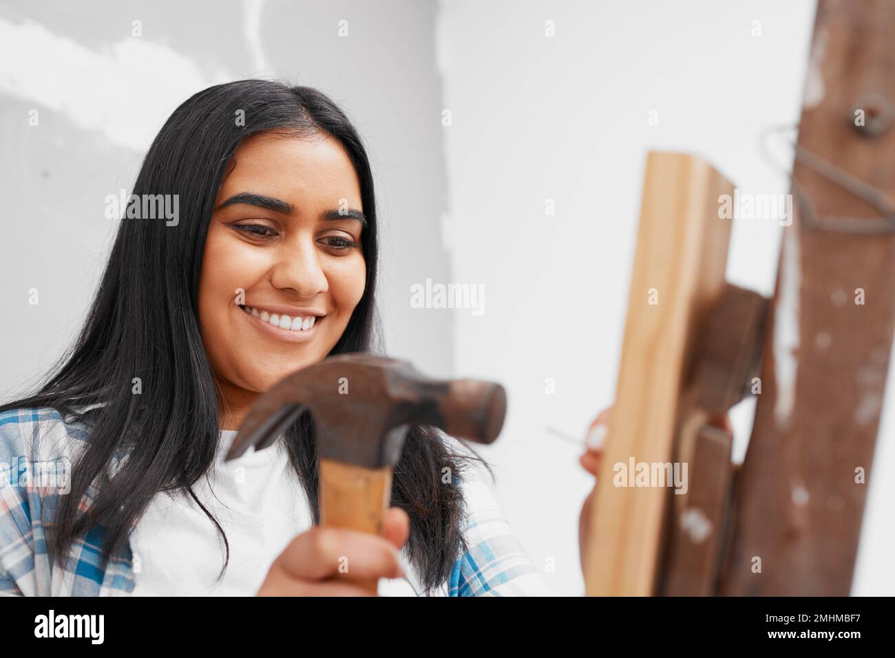 Una giovane donna indiana attraente martella un chiodo in casa di legno fai da te Foto Stock