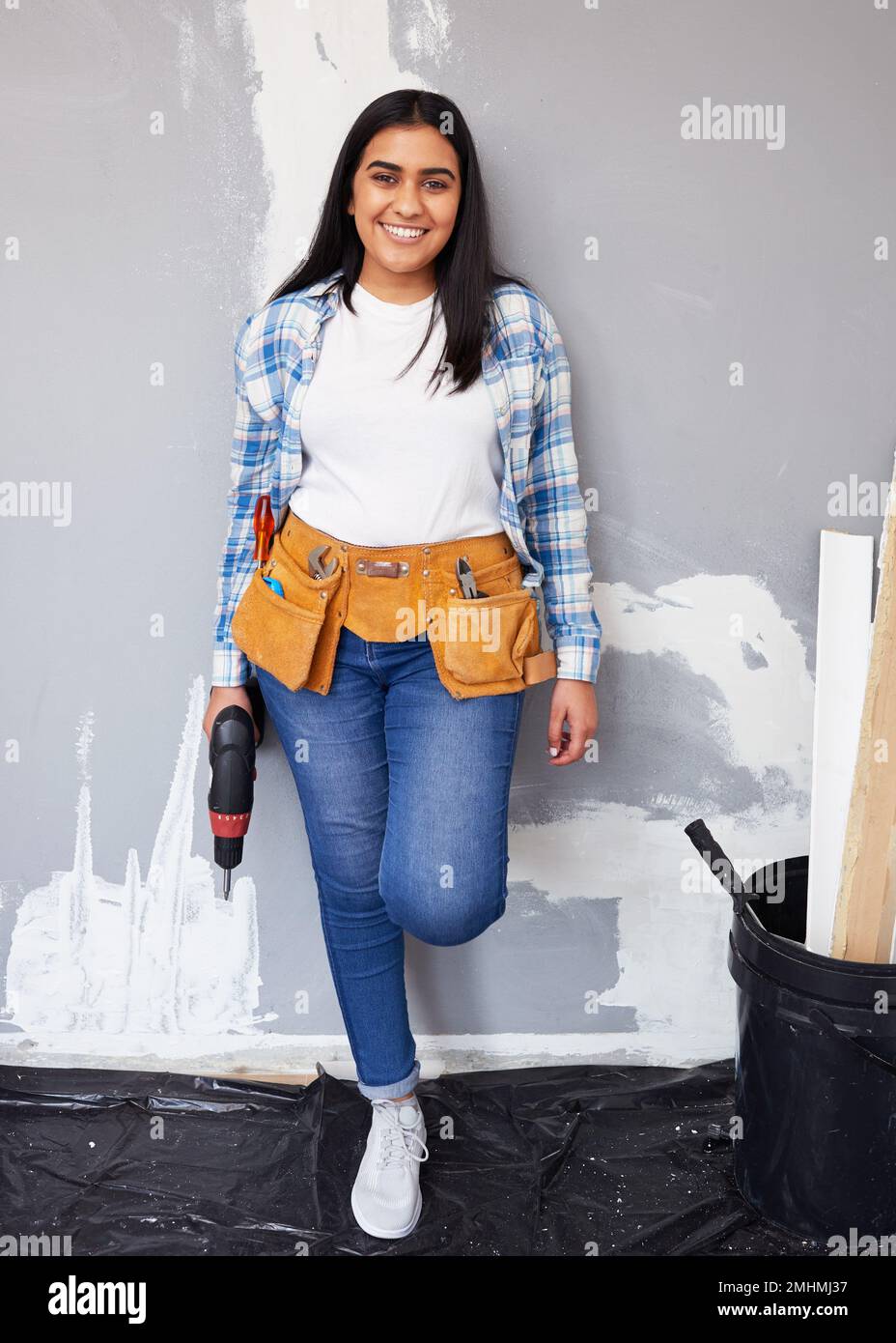 Una giovane donna indiana attraente si appoggia contro la parete facendo il rinnovamento casalingo fai da te Foto Stock