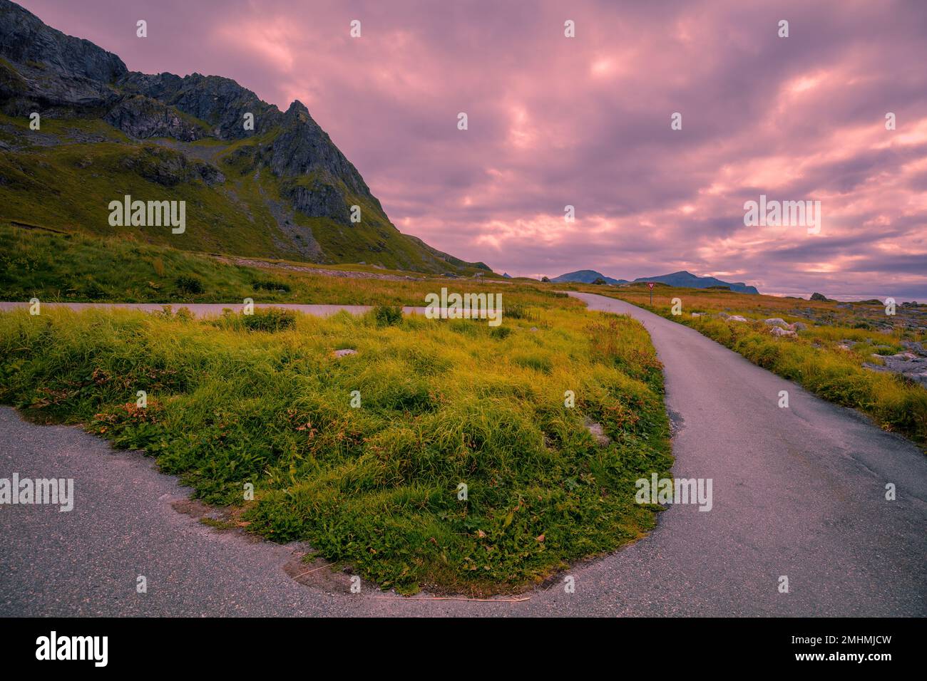 La strada lungo le montagne con un cielo nuvoloso durante il tramonto. Area ricreativa Flakstad, Isole Lofoten, Norvegia Foto Stock