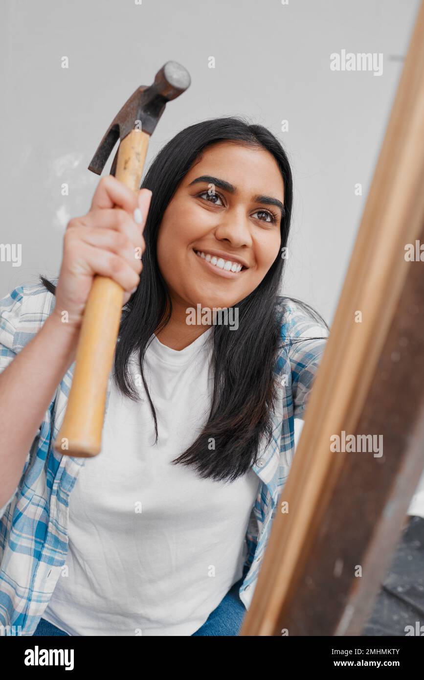 Una giovane donna indiana attraente martella un chiodo in casa di legno fai da te Foto Stock