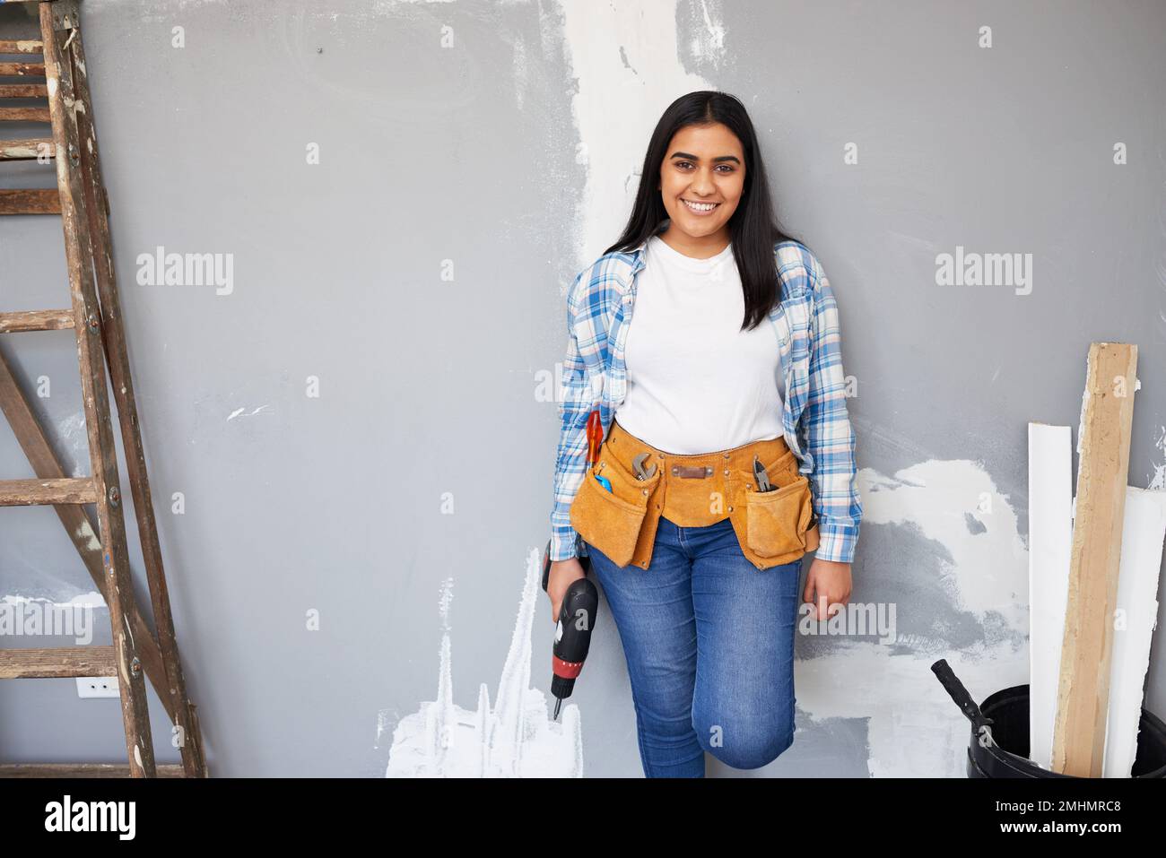 Una giovane donna indiana attraente si appoggia contro la parete facendo il rinnovamento casalingo fai da te Foto Stock