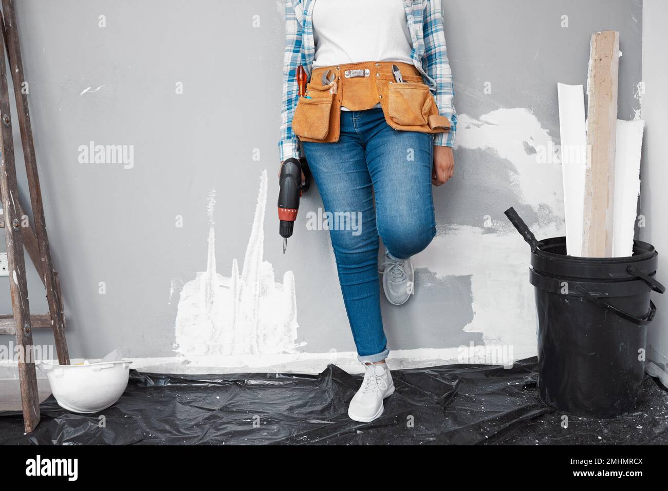 Ripresa ritagliata di una giovane donna che fa il fai da te appoggiandosi contro il muro in fase di ristrutturazione Foto Stock