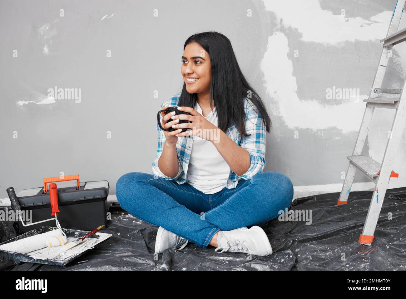 Una giovane donna indiana attraente siede sul pavimento prendendo il caffè pausa dal fai da te Foto Stock