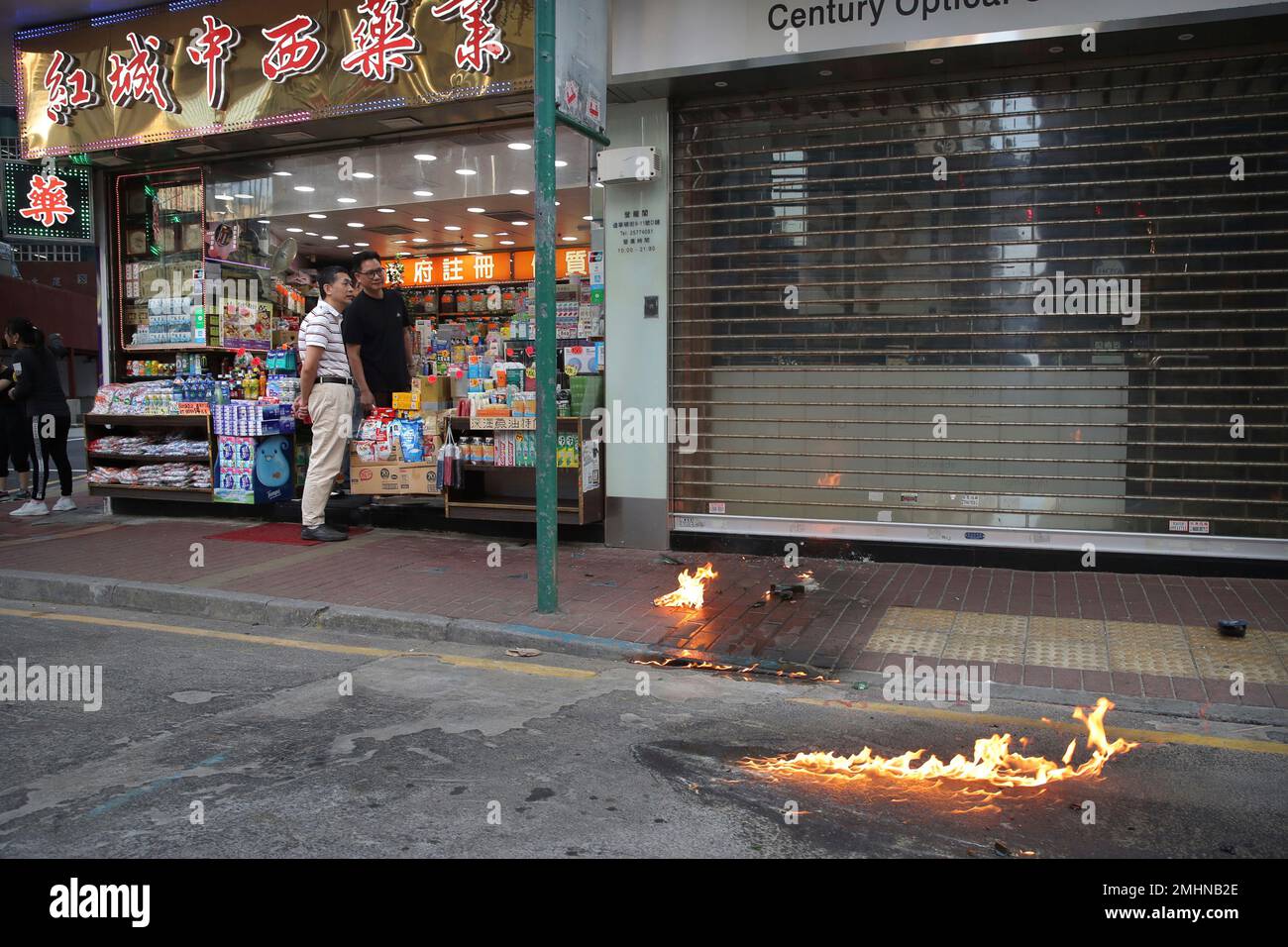 Bystanders look on as fire bombs burn in the street during a protest in Hong Kong, Saturday, Nov. 2, 2019. Hong Kong riot police fired multiple rounds of tear gas and used a water cannon Saturday to break up a rally by thousands of masked protesters demanding meaningful autonomy after Beijing indicated it could tighten its grip on the Chinese territory. (AP Photo/Kin Cheung) Foto Stock