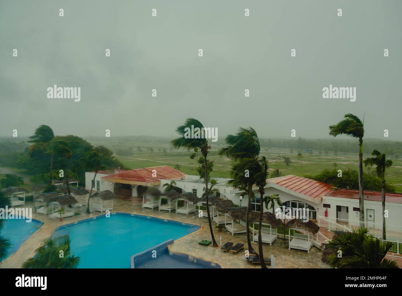 Tempesta, vento, pioggia fuori dalla finestra. Vista sulla piscina e sulle palme dell'hotel. Foto Stock