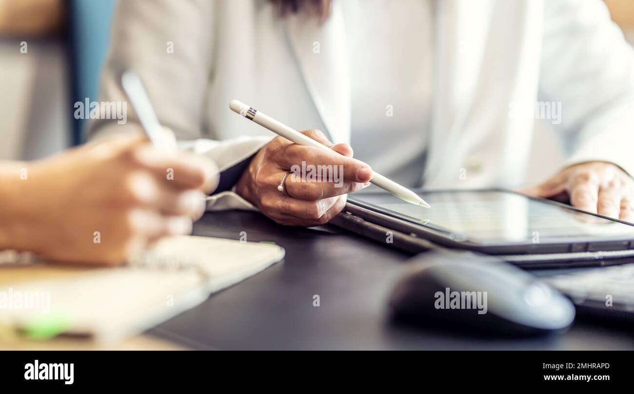 Le mani di due colleghi utilizzano un tablet digitale e un notebook. Un incontro d'affari per discutere di gestione finanziaria, contabilità o financ Foto Stock