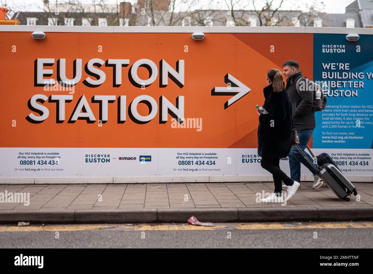 I membri del pubblico camminano oltre le indicazioni che circondano il cantiere per il terminal Euston HS2 di Londra, dove i lavori sono iniziati sei anni fa con oltre £1 miliardi di dollari già spesi. Un'enorme area ad ovest e a nord-ovest della stazione principale esistente è stata ripulita per fare spazio alla ferrovia ad alta velocità, e molte proprietà sono state acquistate. L'inflazione alle stelle significa che la stazione di Euston, riprogettata, potrebbe aprirsi solo nel 2038 e potrebbe essere assestata completamente con treni che si fermano in un nuovo hub a Old Oak Common, nella periferia ovest di Londra. Data immagine: Venerdì 27 gennaio 2023. Foto Stock