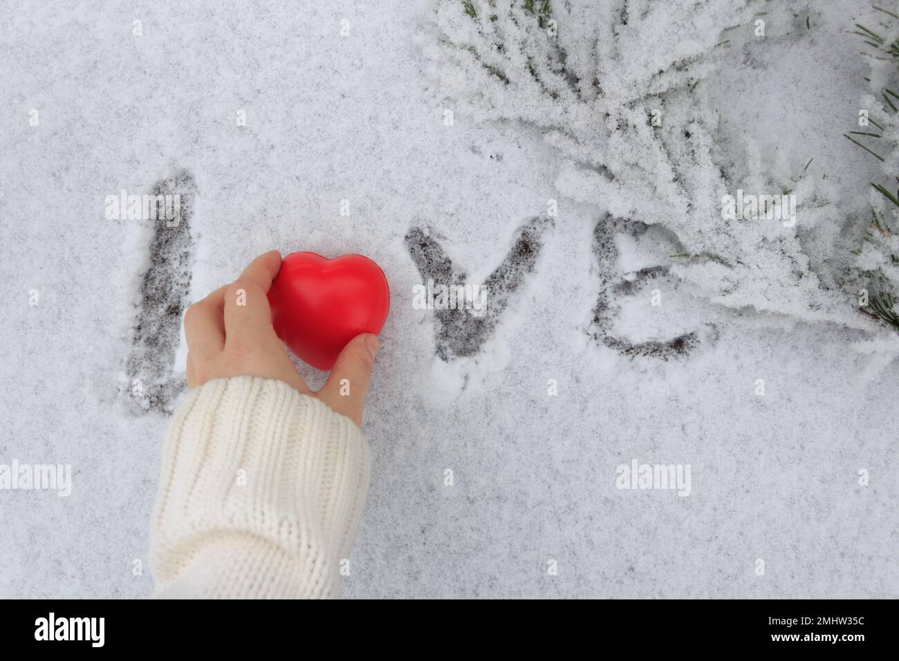 Una figurina a forma di cuore sul palmo di una donna sullo sfondo della parola Amore disegnata sulla neve. Foto Stock