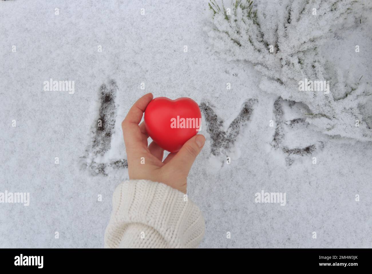 Una figurina a forma di cuore sul palmo di una donna sullo sfondo della parola Amore disegnata sulla neve. Foto Stock