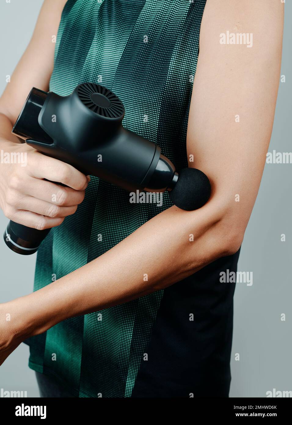 uno sportivo caucasico, in abbigliamento sportivo, sta usando una pistola da massaggio per massaggiare i muscoli del braccio, vicino al gomito Foto Stock