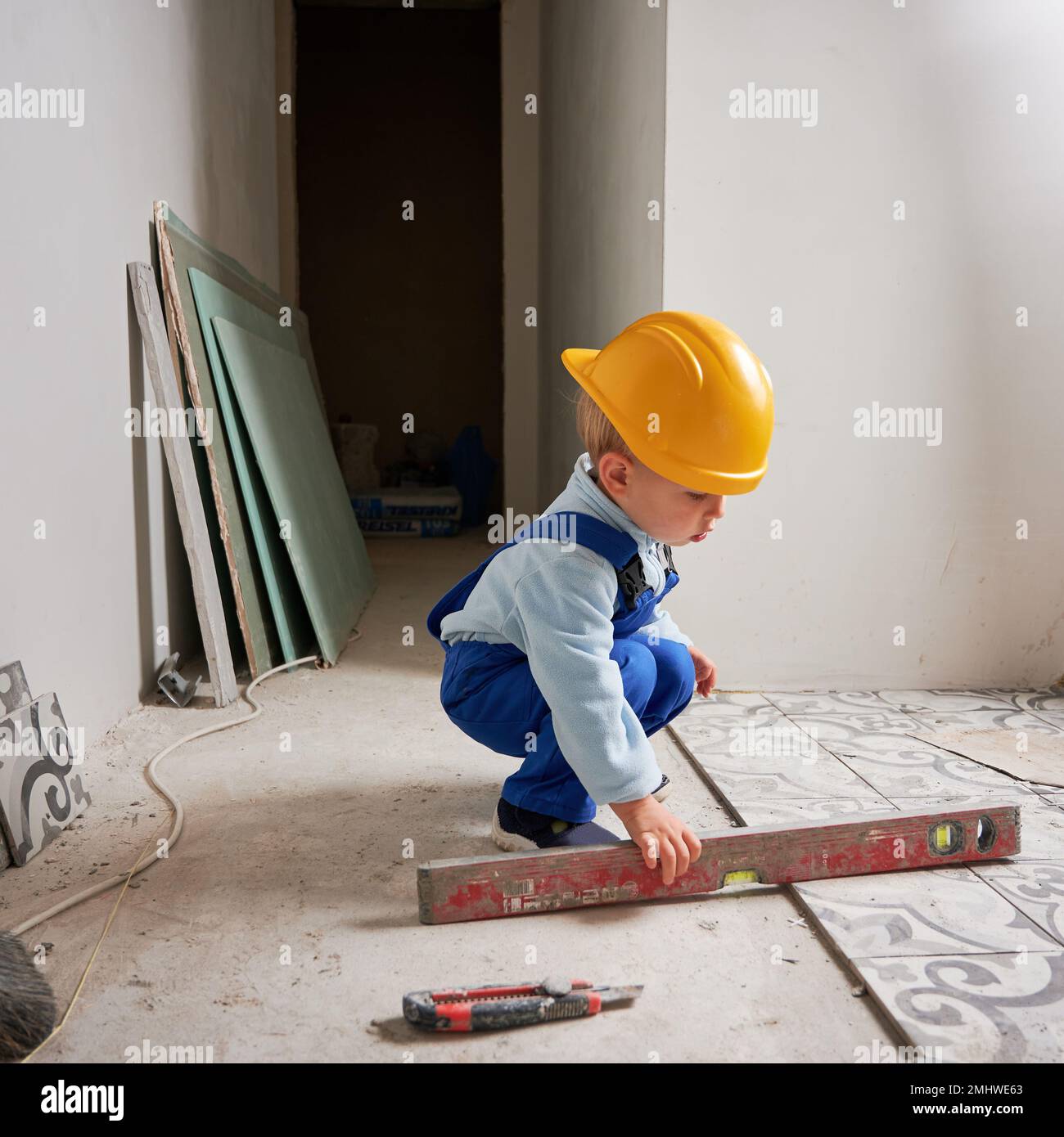 Lavoratore di costruzione di bambino che tiene lo strumento di livella di spirito. Bambini in casco di sicurezza e tute da lavoro che giocano nell'appartamento in fase di ristrutturazione. Foto Stock