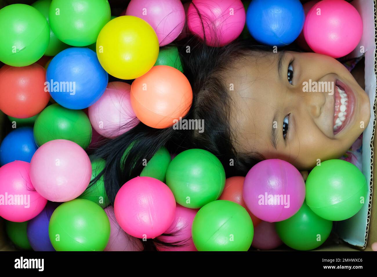 Un primo piano di una bambina del sud-est asiatico con palle giocattolo colorate Foto Stock