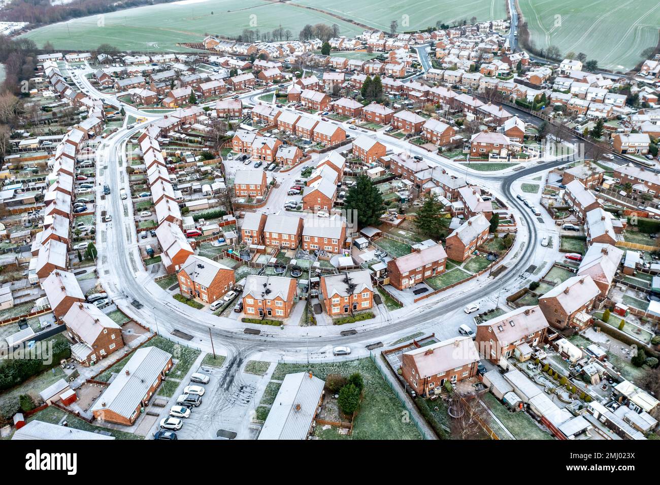 Vista aerea sopra le strade coperte di neve e i tetti di uno sviluppo residenziale suburbano con i proprietari di case che lottano per permettersi le bollette di energia durante Foto Stock