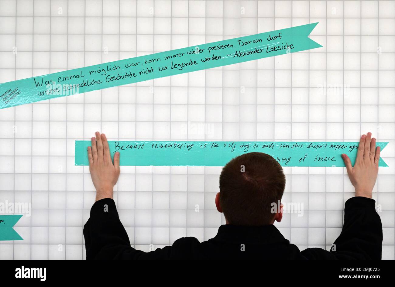 27 gennaio 2023, Brandeburgo, Oranienburg: Un giovane greco ha bloccato un nastro con un detto che aveva scritto sul muro all'interno della 'Stazione Z' del Sachsenhausen Memorial and Museum. Durante la manifestazione congiunta del Parlamento di Stato del Brandeburgo e del memoriale, per la prima volta, invece di fare una corona, è stata condotta un'azione di "nastro d'arte" con la domanda "perché vi ricordate oggi?”. Sul nastro dell'uomo c'è il detto: 'Perché ricordare è l'unico modo per assicurarsi che ciò non accada di nuovo'. Oltre ai visitatori del memoriale, più di 90 persone avevano risposto al memo Foto Stock