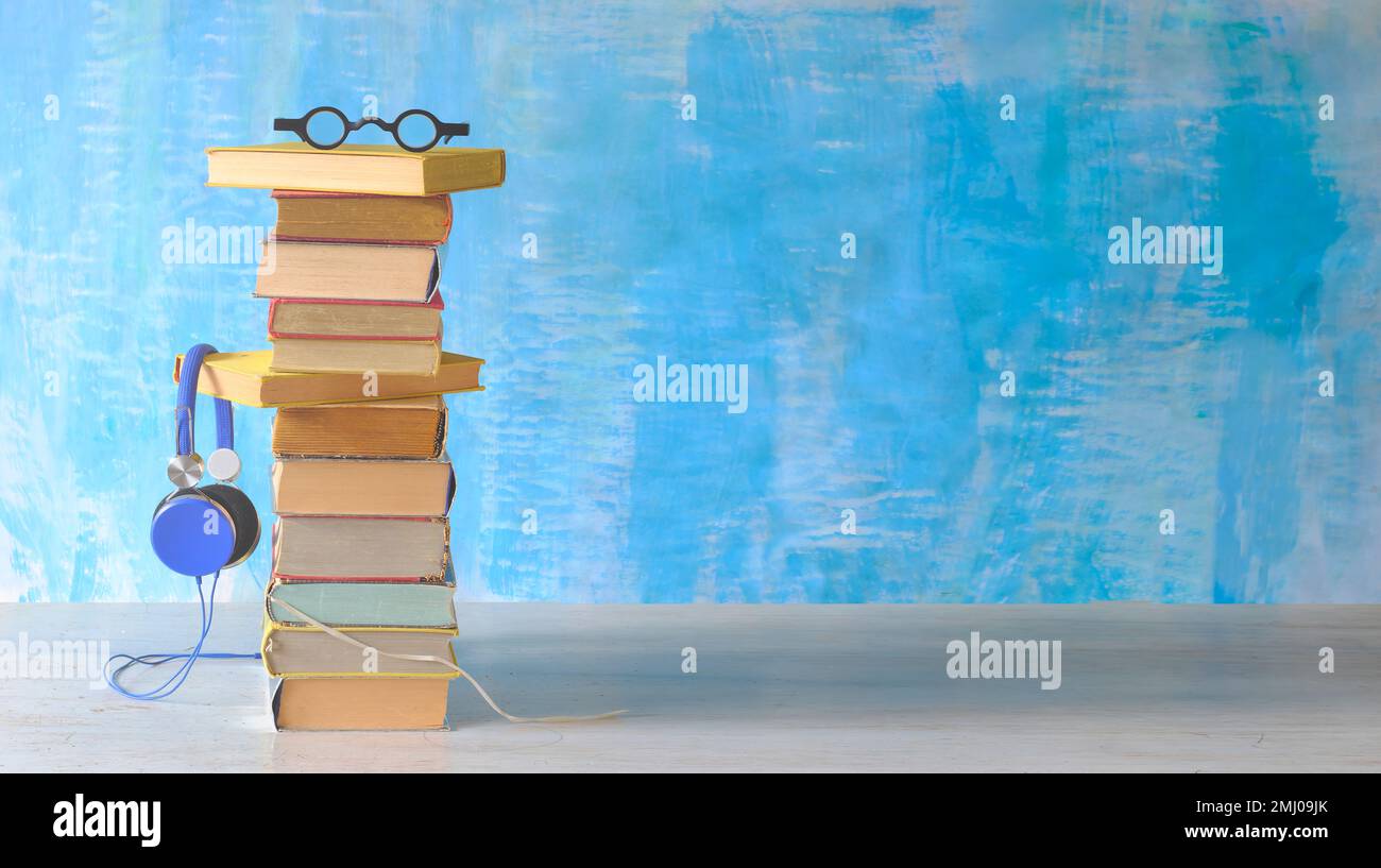 concetto di audiolibro con grande pila di occhiali da libro e cuffie vintage, sfondo di vernice blu Foto Stock