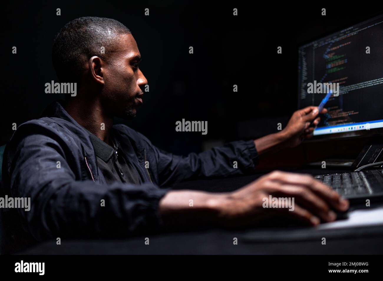 Maschio nero che legge il codice scritto sul monitor nella stanza buia Foto Stock