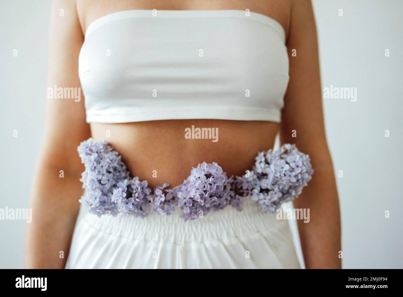 Primo piano di bella giovane donna curvy in un reggiseno bianco e pantaloni con fiori di lilla. Femmina bianca Bodypositive. Accettazione del corpo e concetto di diversità Foto Stock