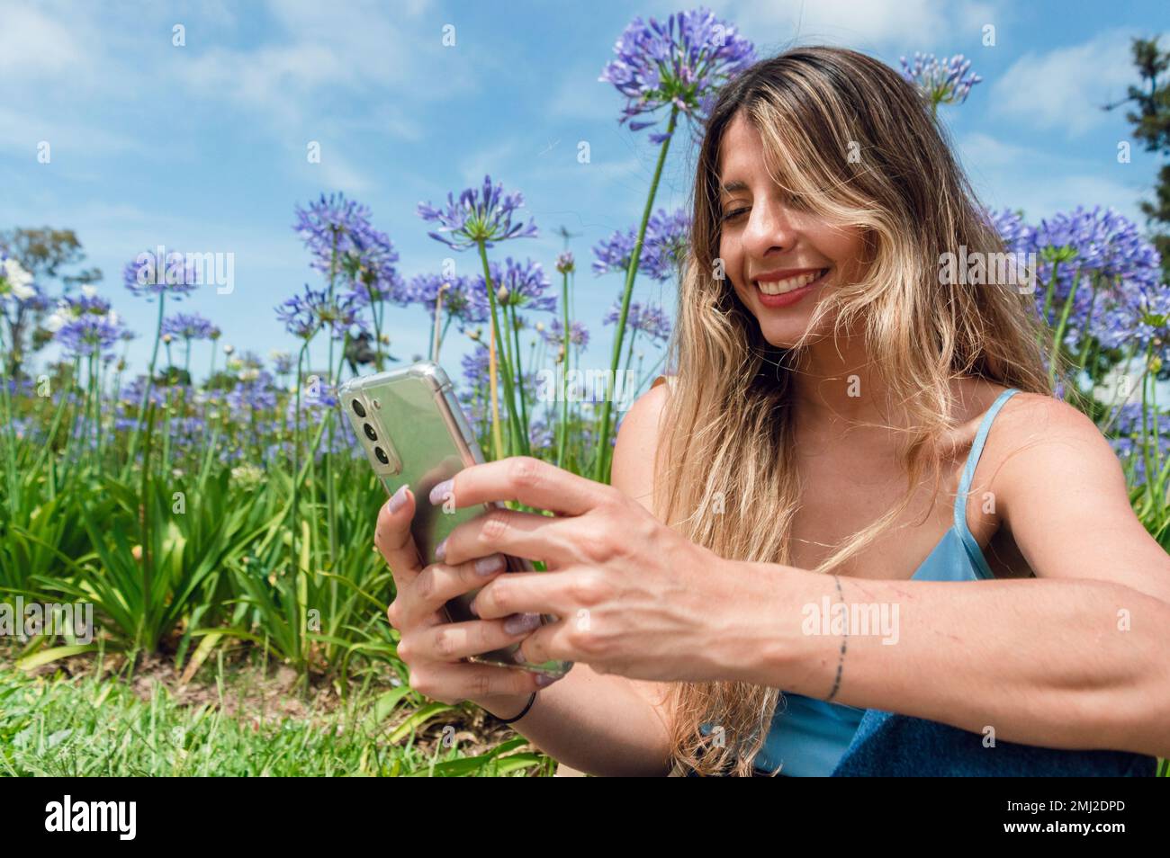ritratto di giovane donna latina di etnia colombiana, capelli lunghi, abiti blu, sorridente, divertito seduto nel parco a riposo con il telefono, con volata Foto Stock