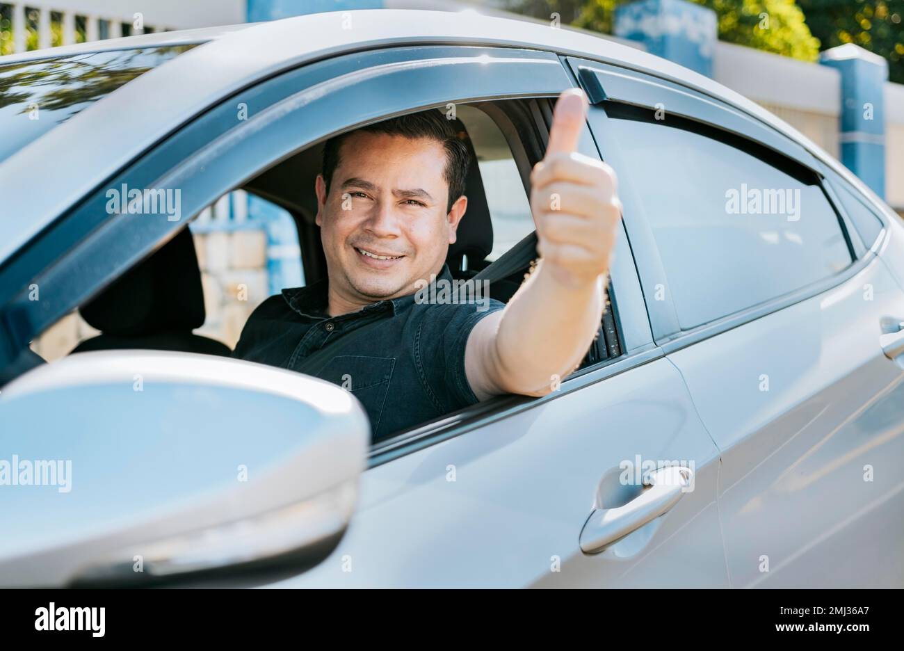 L'uomo nella sua auto che dà i pollici in su, driver felice che dà i pollici in su. Conducente soddisfatto che mostra il pollice in su. Concetto di proprietario soddisfatto dell'automobile Foto Stock