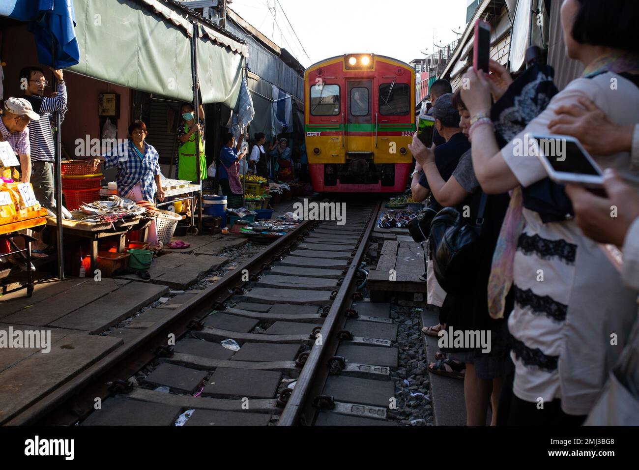 Folla di persone nel mercato Rom Hup mentre un treno locale si fa strada attraverso il mercato ferroviario ( ตลาดร่มหุบ ) Thailandia Foto Stock