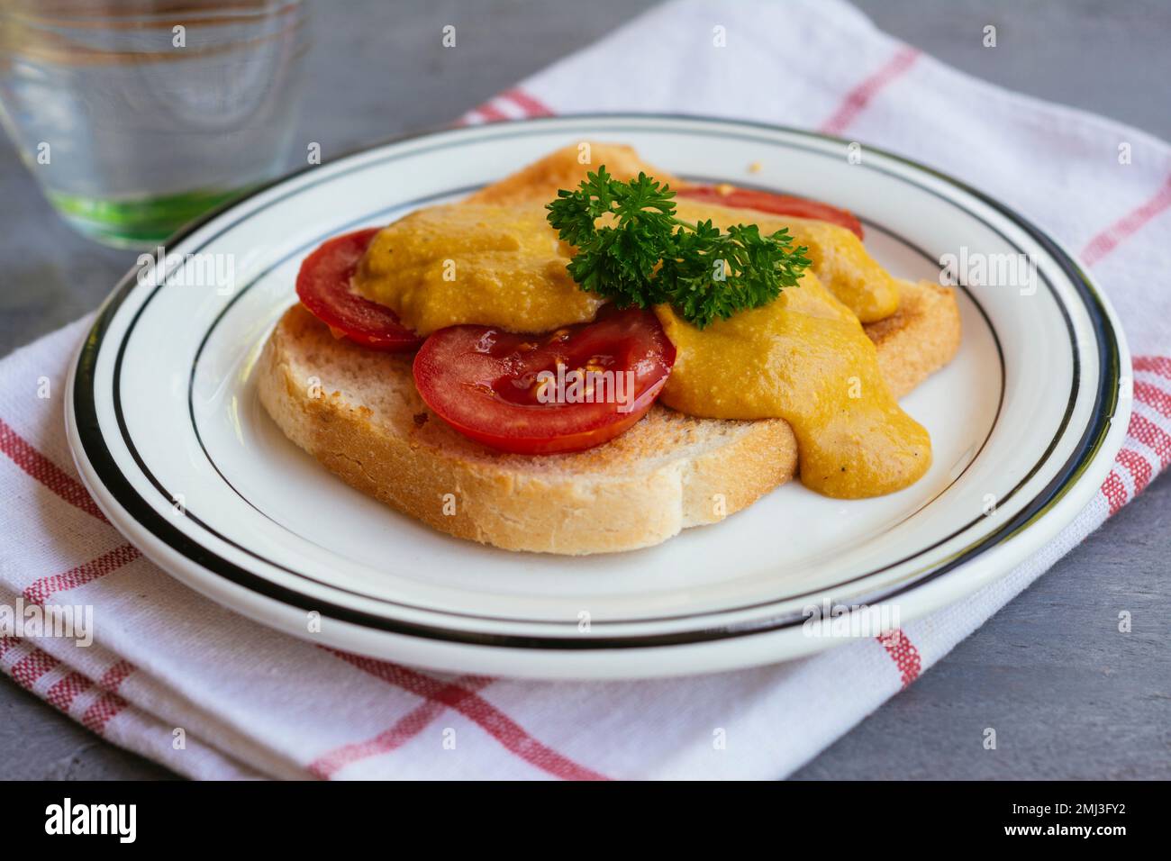 Ravebito vegano gallese - pane tostato e pomodori con una salsa di formaggio vegano a base di noci di anacardi e carote. Foto Stock