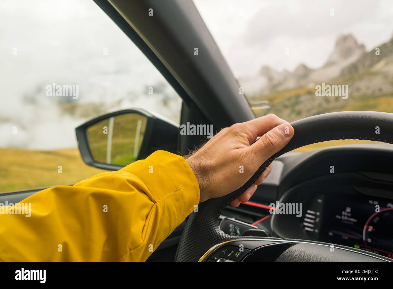 L'uomo guida l'auto in autostrada contro le Alpi italiane giganti circondate dalla nebbia. Le mani del conducente che tiene il volante e la vista panoramica all'esterno del finestrino Foto Stock