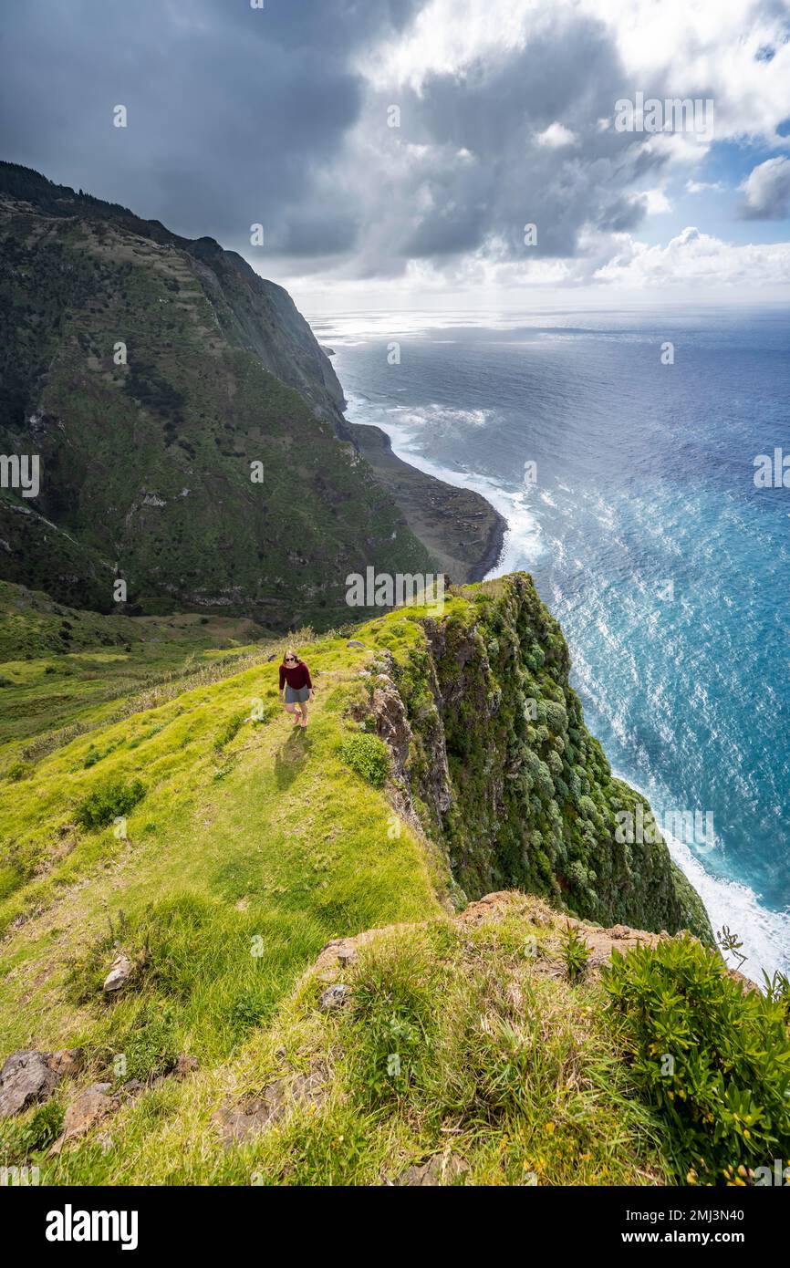 Giovane donna che gode di vista di scogliere e mare, paesaggio costiero, punto di vista Ponta da Leideira, vicino a Calhau das Achadas, Madeira, Portogallo Foto Stock