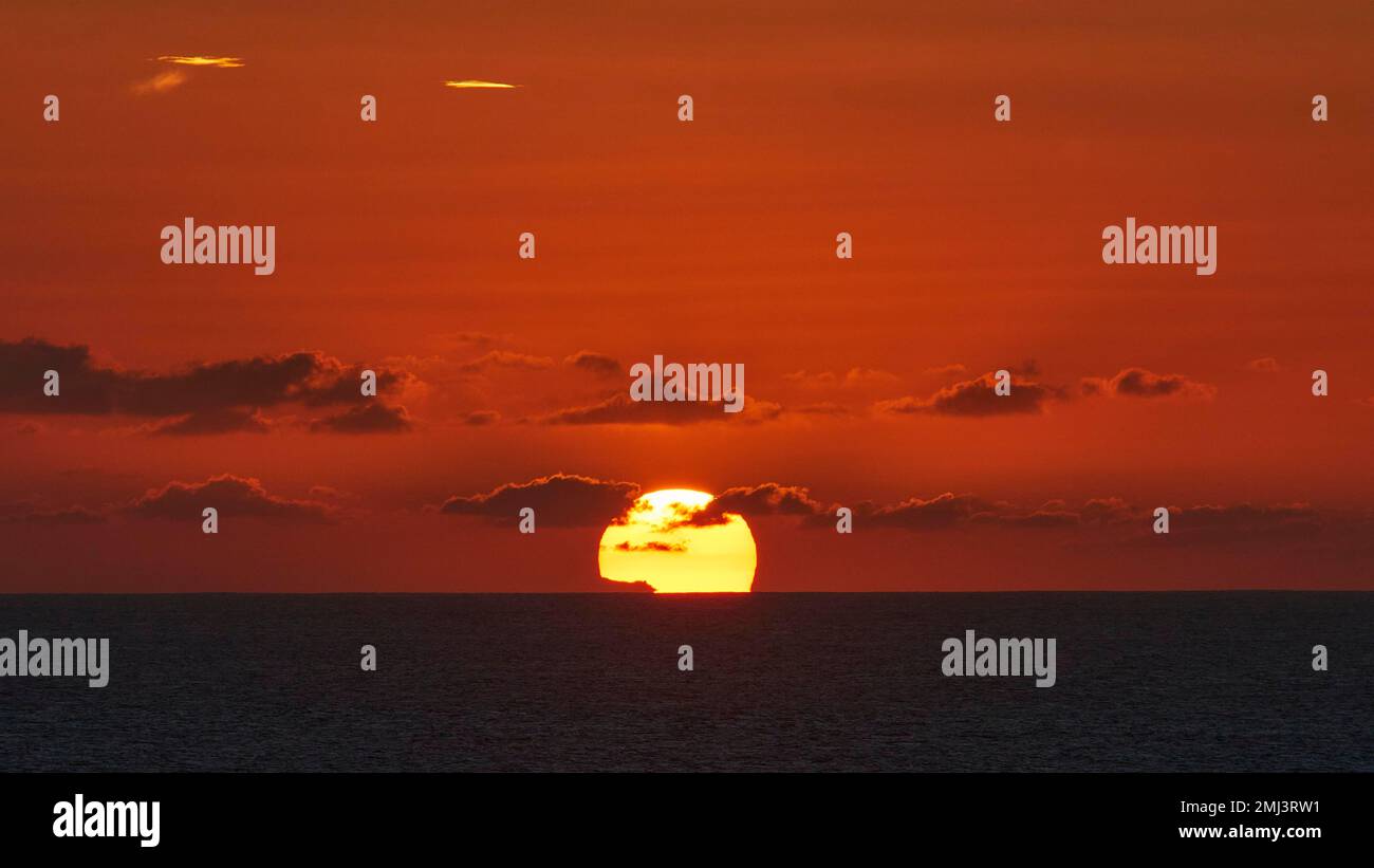 Punta de Toston, tramonto, grande disco del sole che affonda nel mare, mare scuro, cielo rosso-arancio, nuvole grigie, costa occidentale, Fuerteventura, Canarie Foto Stock
