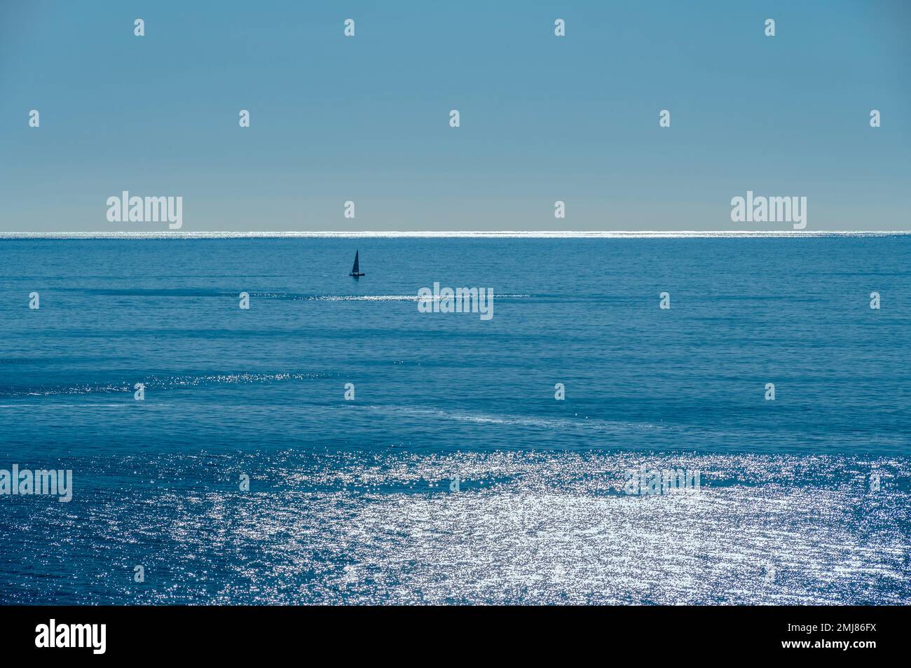 Barca a vela circondata dall'oceano blu e dal cielo. Foto Stock