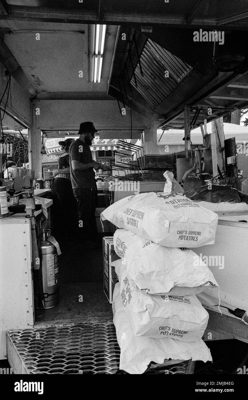 Un cuoco lavora all'interno di un camion di cibo preparando French Fries con diversi sacchetti di patate fresche in primo piano del rimorchio alla fiera di Deerfield, N Foto Stock
