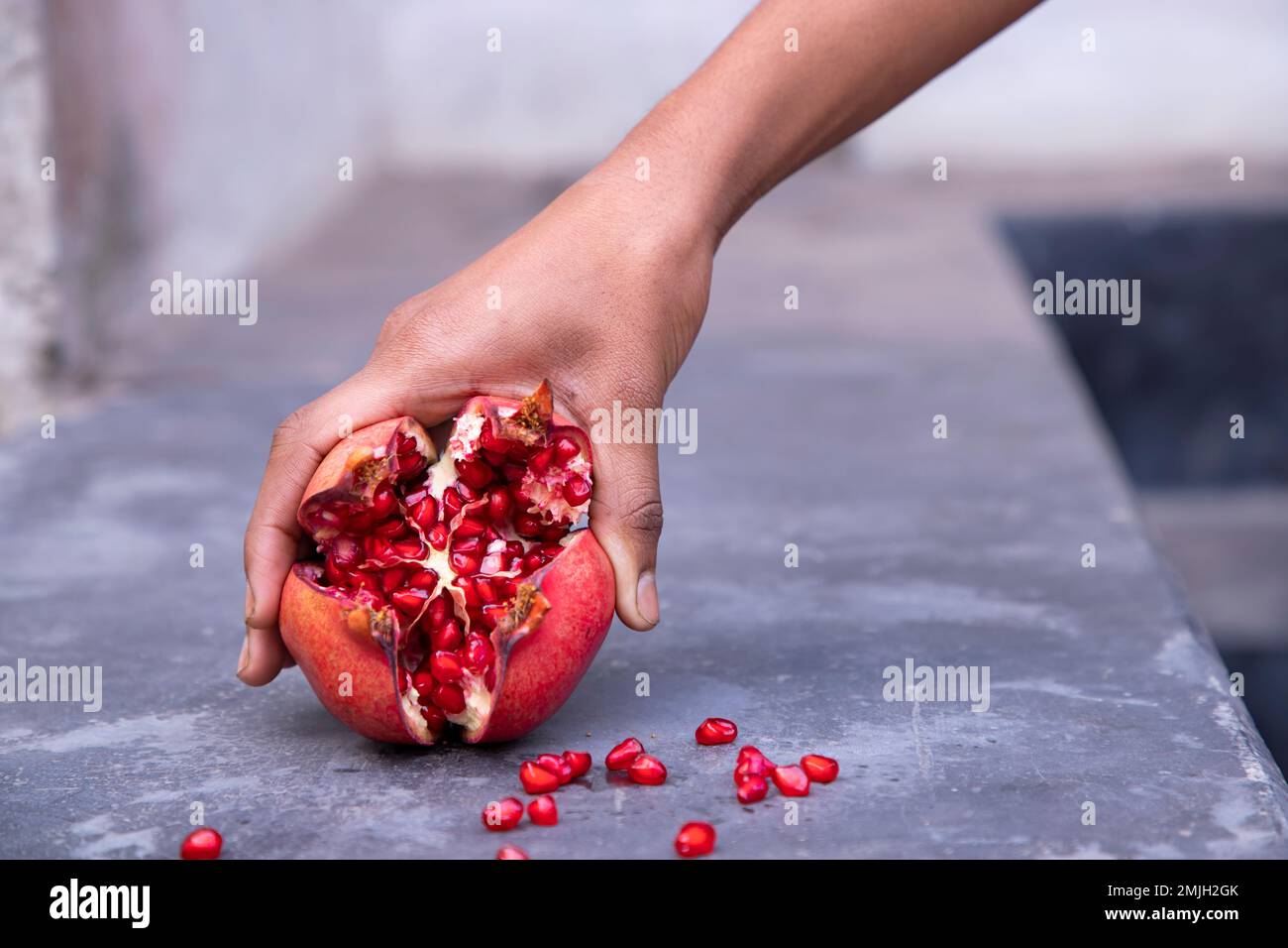 Frutto di melograno maturo in mano donna su fondo di cemento Foto Stock