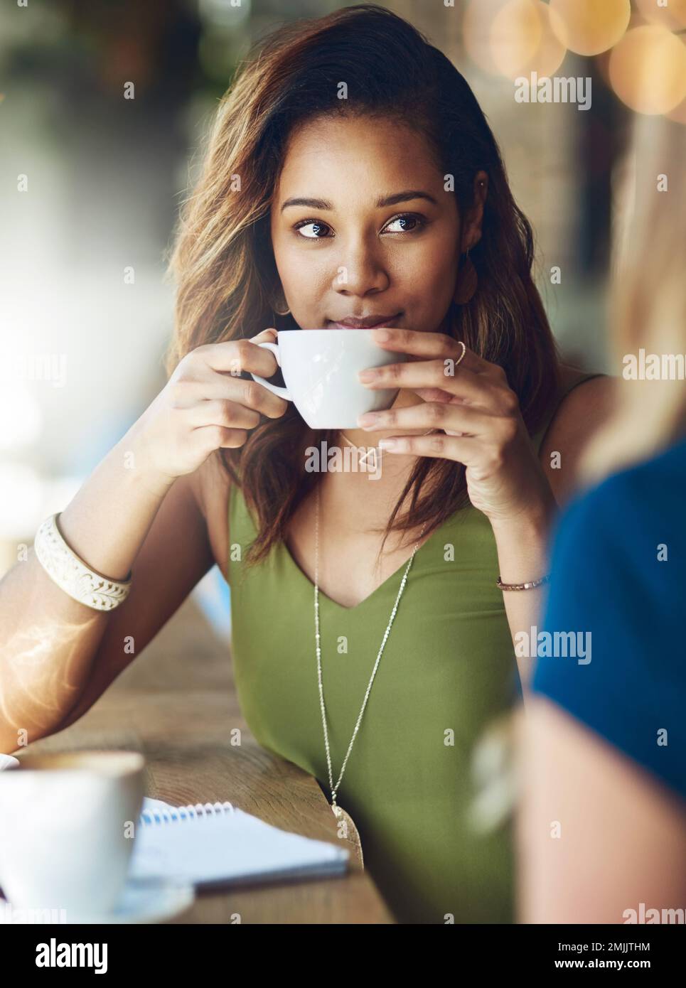Con il caffè in mano, im tutte le orecchie. una donna che chiacchiera con la sua amica in un bar. Foto Stock