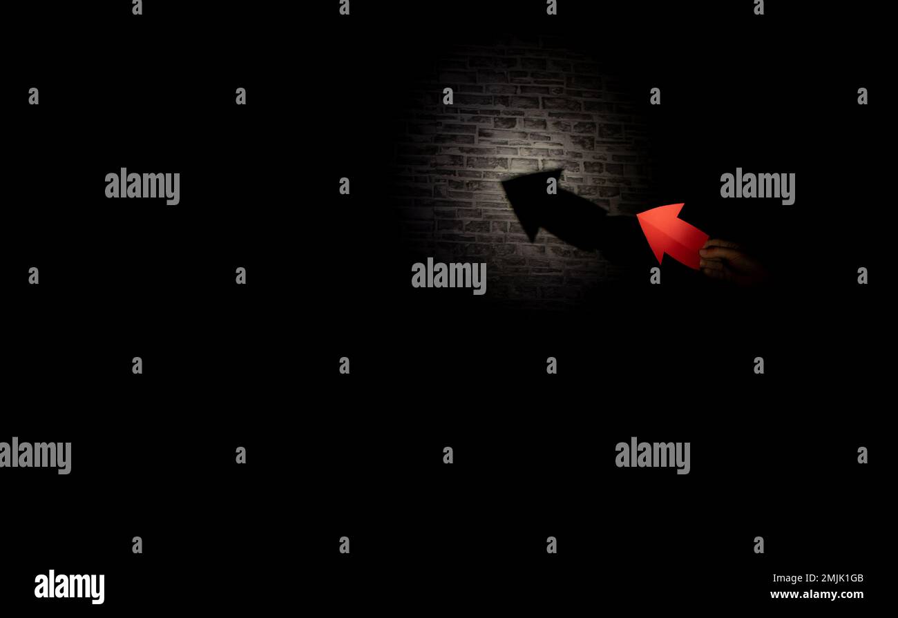 freccia su carta illuminata da una lanterna crea un'ombra di una freccia su uno sfondo scuro Foto Stock