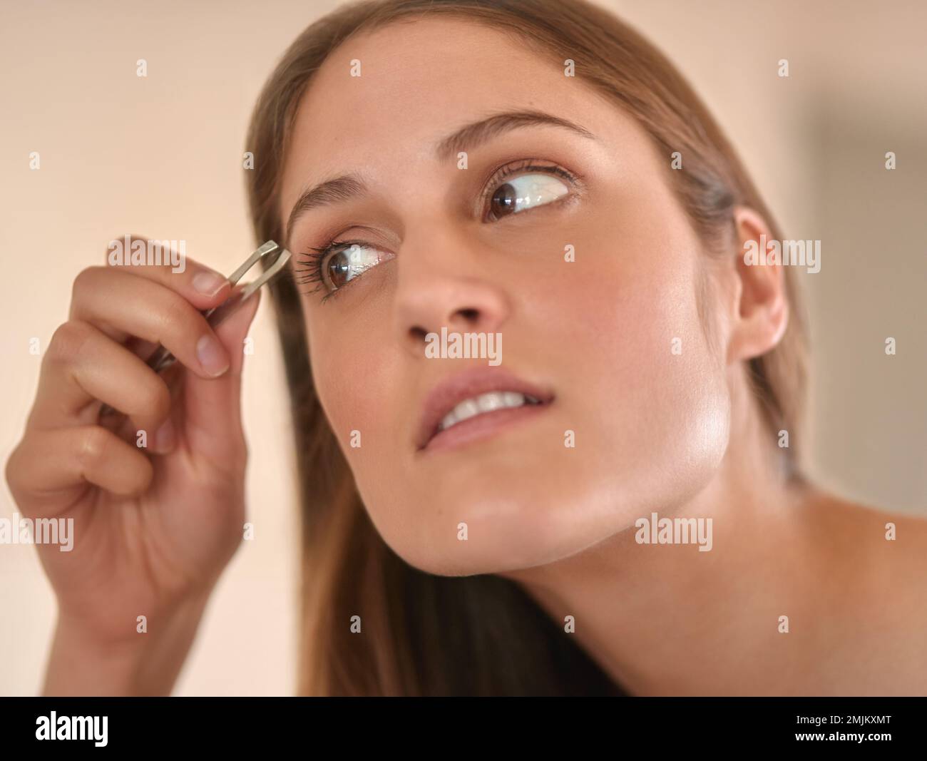 Modellare le sopracciglia alla perfezione. una giovane donna che le strappa le sopracciglia con un paio di pinzette. Foto Stock