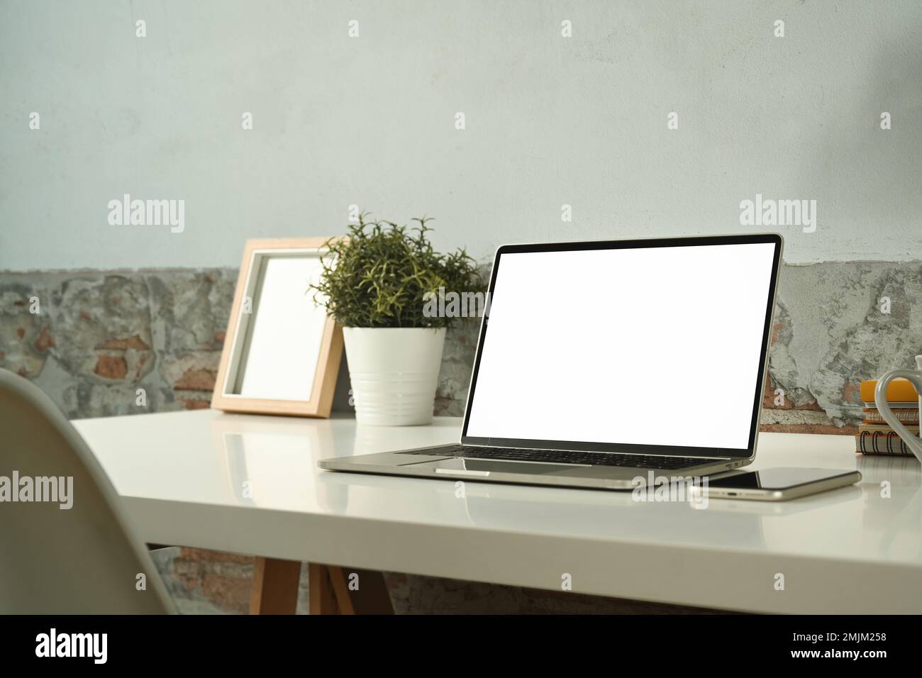 Ambiente di lavoro confortevole con computer portatile, smartphone, cornice per immagini e pianta in vaso in un tavolo bianco Foto Stock
