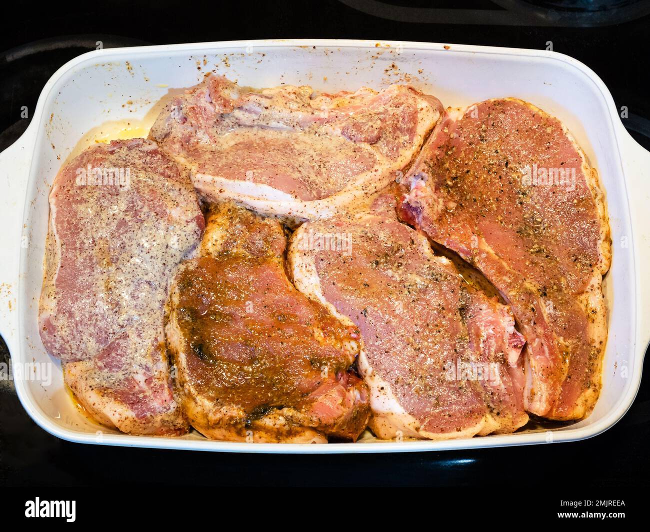 diverse braciole di maiale crudo con condimento e olio in ceramica da forno piatto in cucina casa Foto Stock