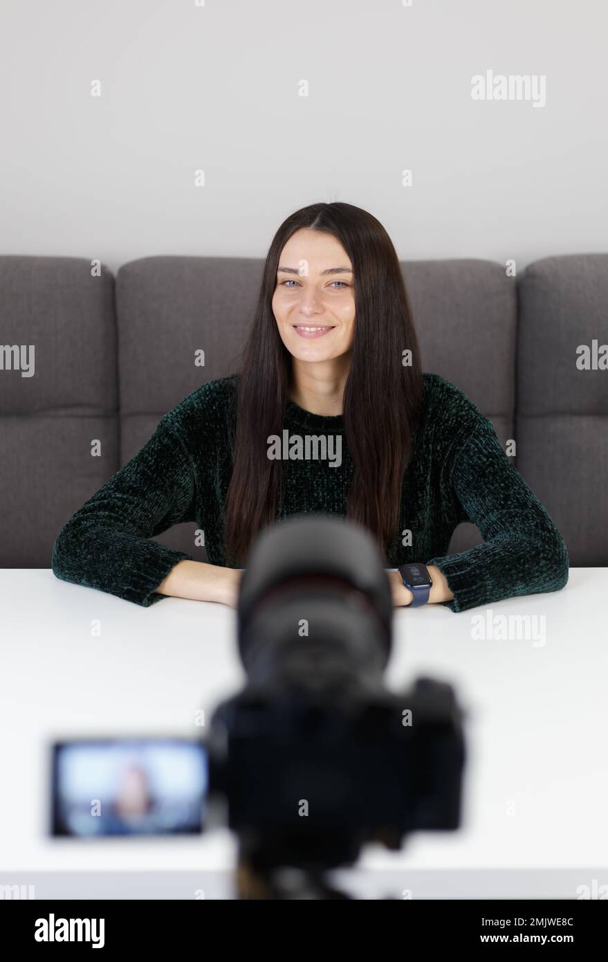 Video blogger femmina parla con un sorriso sulla fotocamera. Giovane donna brunette film video blog a casa Foto Stock