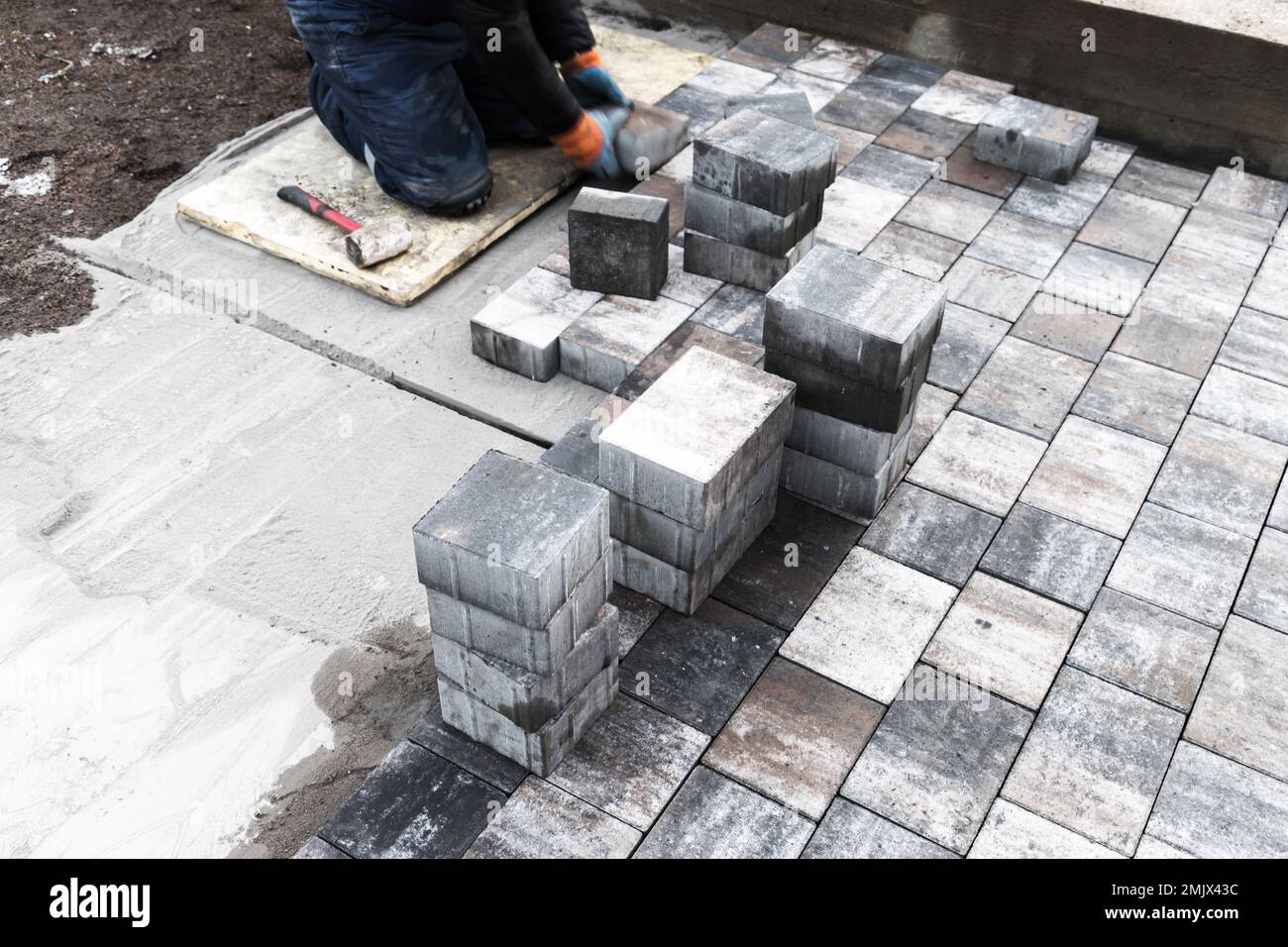 Lavoratore che posa lastre di pavimentazione grigie su base di cemento. Lavori di pavimentazione stradale in corso. Foto di sfondo con messa a fuoco selettiva Foto Stock