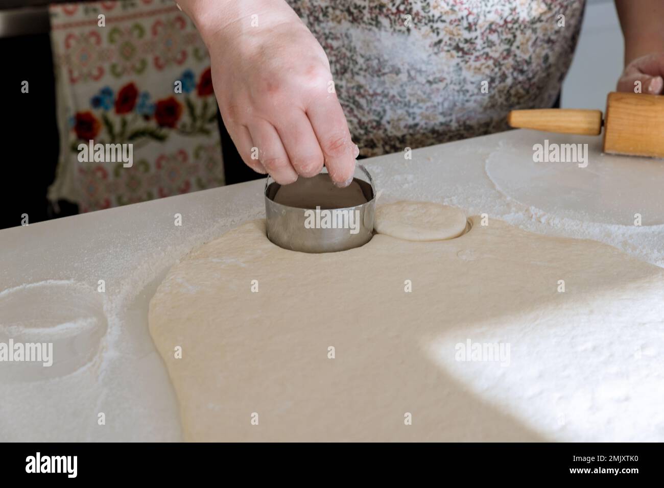 Pasta cruda fatta in casa per ciambelle tagliare l'impasto in pezzi tondi con il perno sul tavolo di lavoro del forno Foto Stock