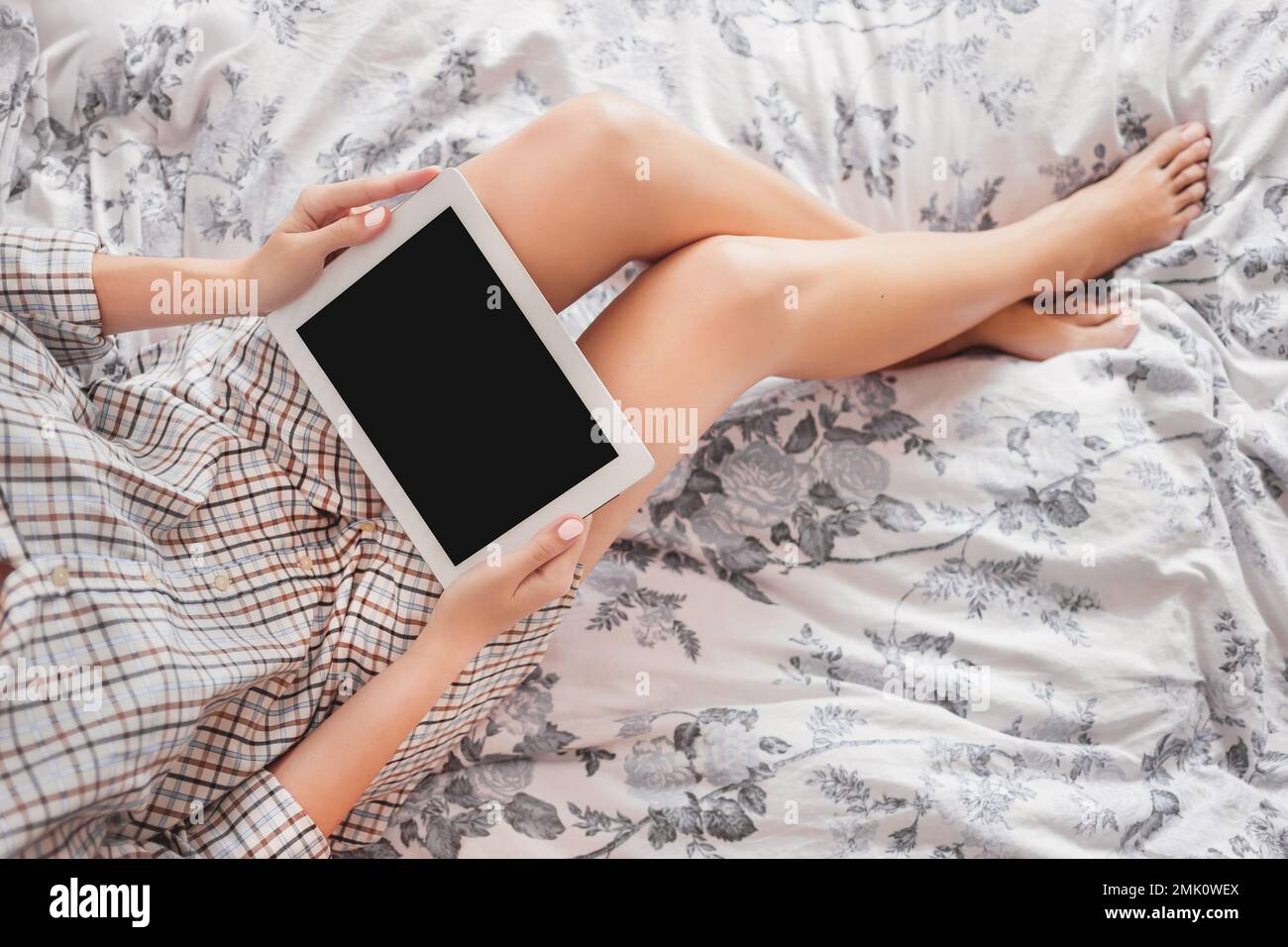 Vista dall'alto su una donna in pigiama con tablet digitale. Controllare e-mail e leggere notizie sul gadget a letto. Schermo nero trasparente del dispositivo elettronico. Foto Stock