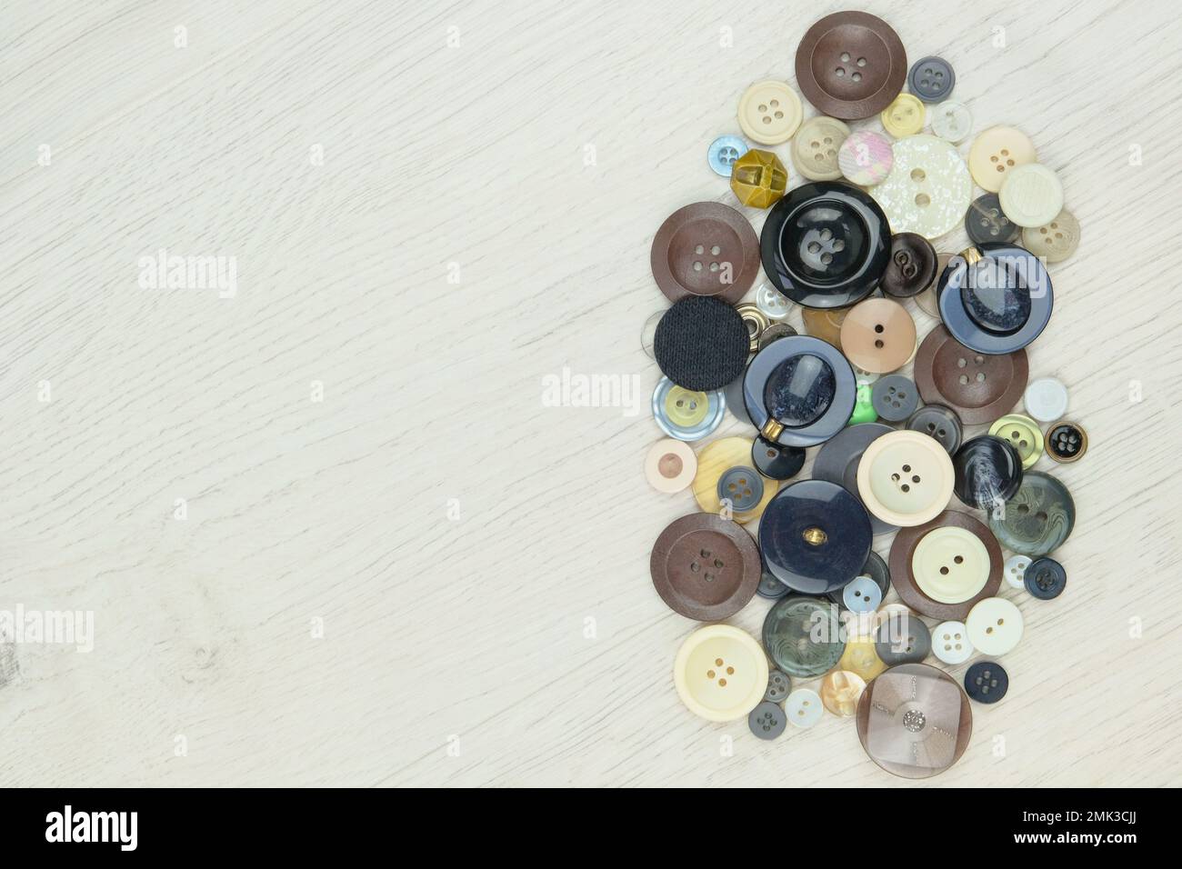 Varietà di bottoni di diversi colori e dimensioni su uno sfondo di legno chiaro. Vista dall'alto. Spazio per il testo. Foto Stock