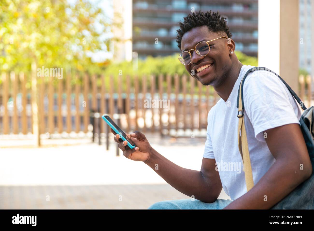 Ritratto di giovane studente seduto nel parco, utilizzando il suo telefono cellulare e guardando la fotocamera - sorriso uomo felice - concetto di istruzione Foto Stock