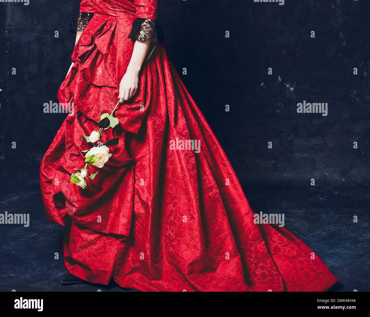 Donna vestita con un romantico abito rosso, tenendo in mano un fiore di camelia. Foto Stock