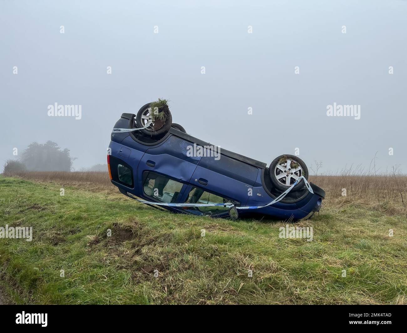 Un'auto hatchback Suzuki rovesciata blu che riposa sul suo tetto dopo essersi schiantata da una strada sull'erba Foto Stock